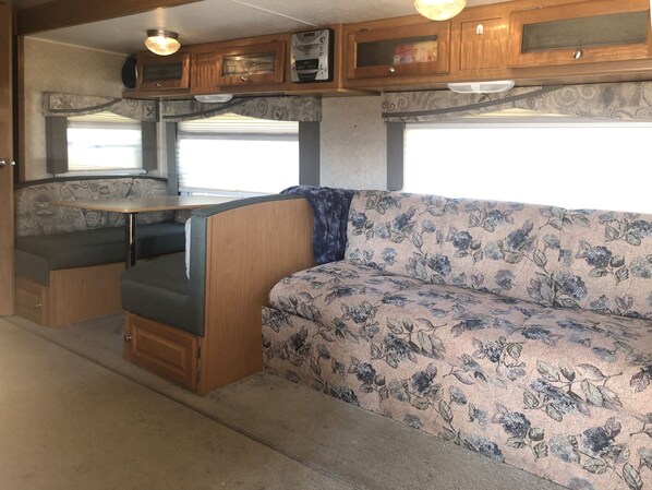 Een compact camperinterieur met een kitchenette, een eettafel en een bank.