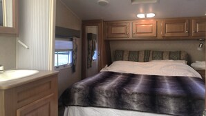 A bedroom with a bed, a vanity with a mirror, wooden cabinets, and a ceiling vent. - Misty Haven Farm (Ladysmith)