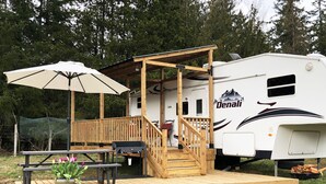 A recreational vehicle with a wooden deck, a picnic table, and a potted plant. - Misty Haven Farm (Ladysmith)
