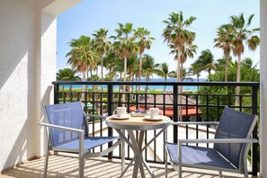 A balcony with two chairs and a small table, overlooking a beach with palm trees and a clear sky. - Marriott Ocean Pointe, Oceanside, Kitchen, Access to Resort Amenities (Palm Beach Shores)