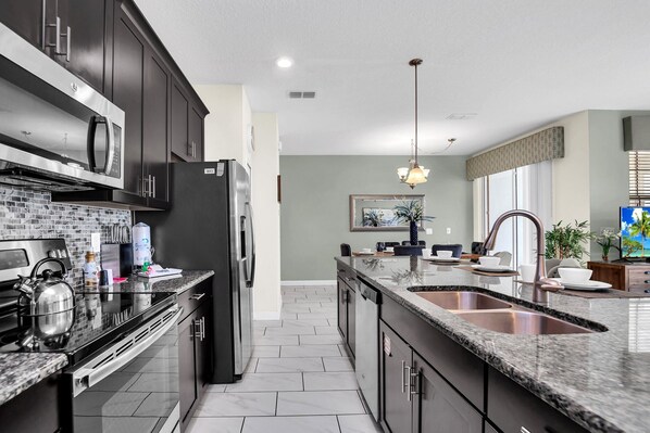 A modern kitchen with dark cabinetry, stainless steel appliances, and a granite countertop.
