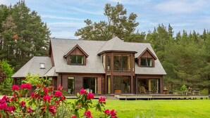 Een modern herenhuis met twee verdiepingen en een ruim terras, omgeven door weelderige begroeiing en bloeiende planten.