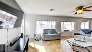 A modern living room with a flat-screen TV, two grey sofas, a coffee table, and a ceiling fan. - Putting Green, Pool & Spa: Home in Queen Creek! (Queen Creek)