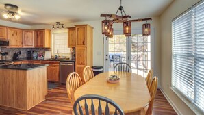 A kitchen with wooden cabinets, a central island, and a dining area with a table and chairs. - Lyles Peaceful Creekside Home: Hot Tub & Fire Pit (Lyles)