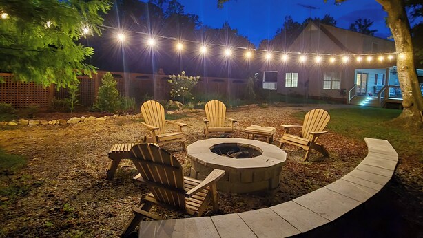 A backyard with a fire pit, outdoor seating, and string lights. - Lyles Peaceful Creekside Home: Hot Tub & Fire Pit (Lyles)