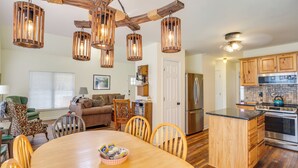 A modern kitchen with wooden cabinets, a central island, and a dining area with a round table and chairs. - Lyles Peaceful Creekside Home: Hot Tub & Fire Pit (Lyles)