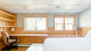 Une chambre avec des lambris en bois, un bureau, une chaise, un lit et deux fenêtres.