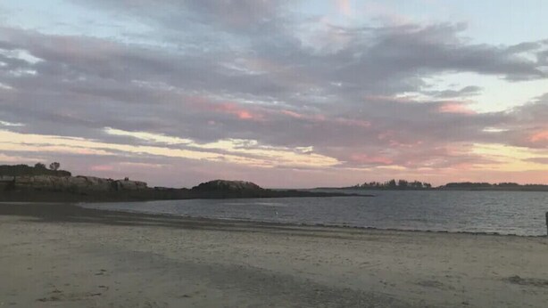 Une plage avec une mer calme et un ciel au coucher du soleil.