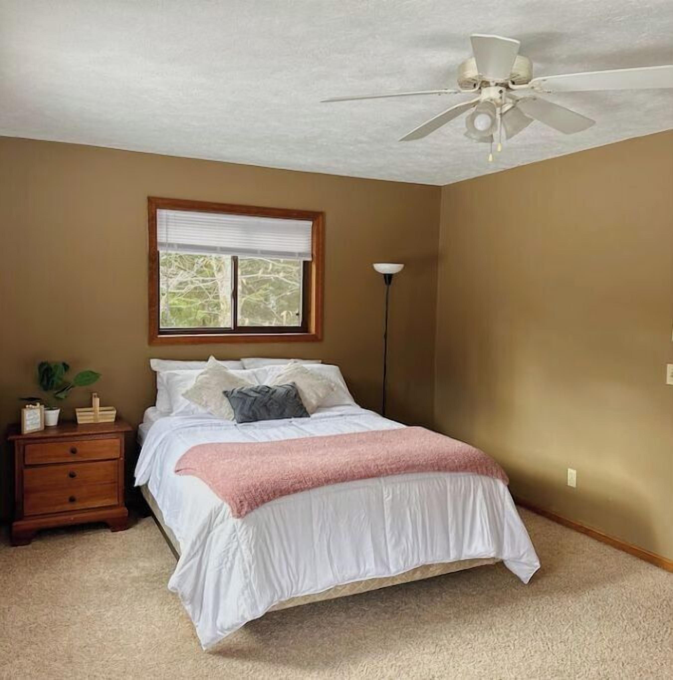A bedroom with a bed, a nightstand, a lamp, and a ceiling fan.