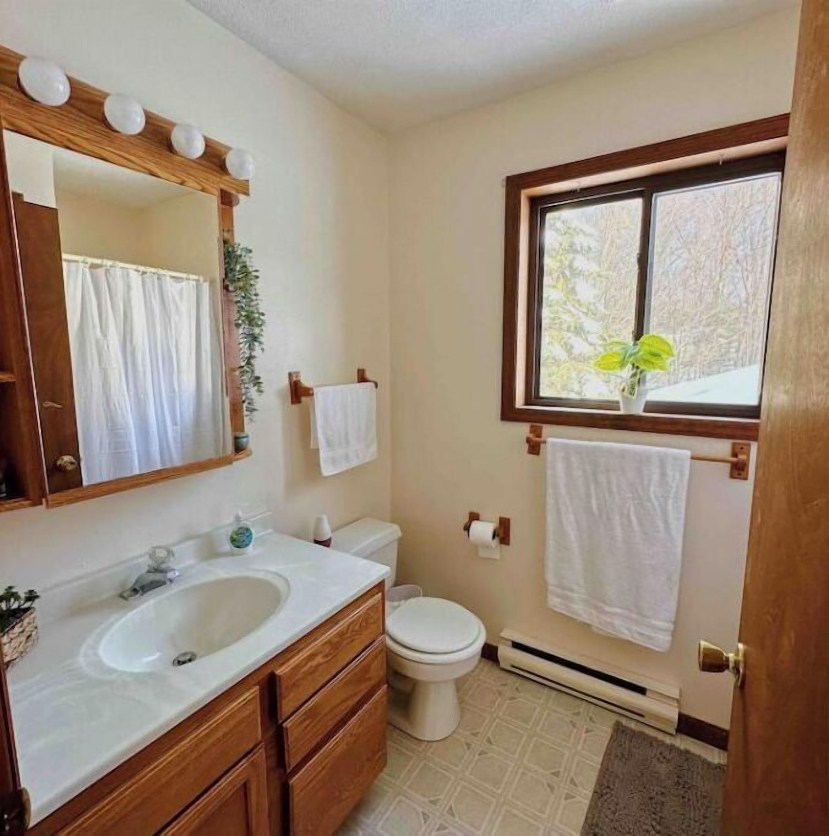 Ein Badezimmer mit Waschbecken, Spiegel, Toilette und einem Fenster mit Pflanze.