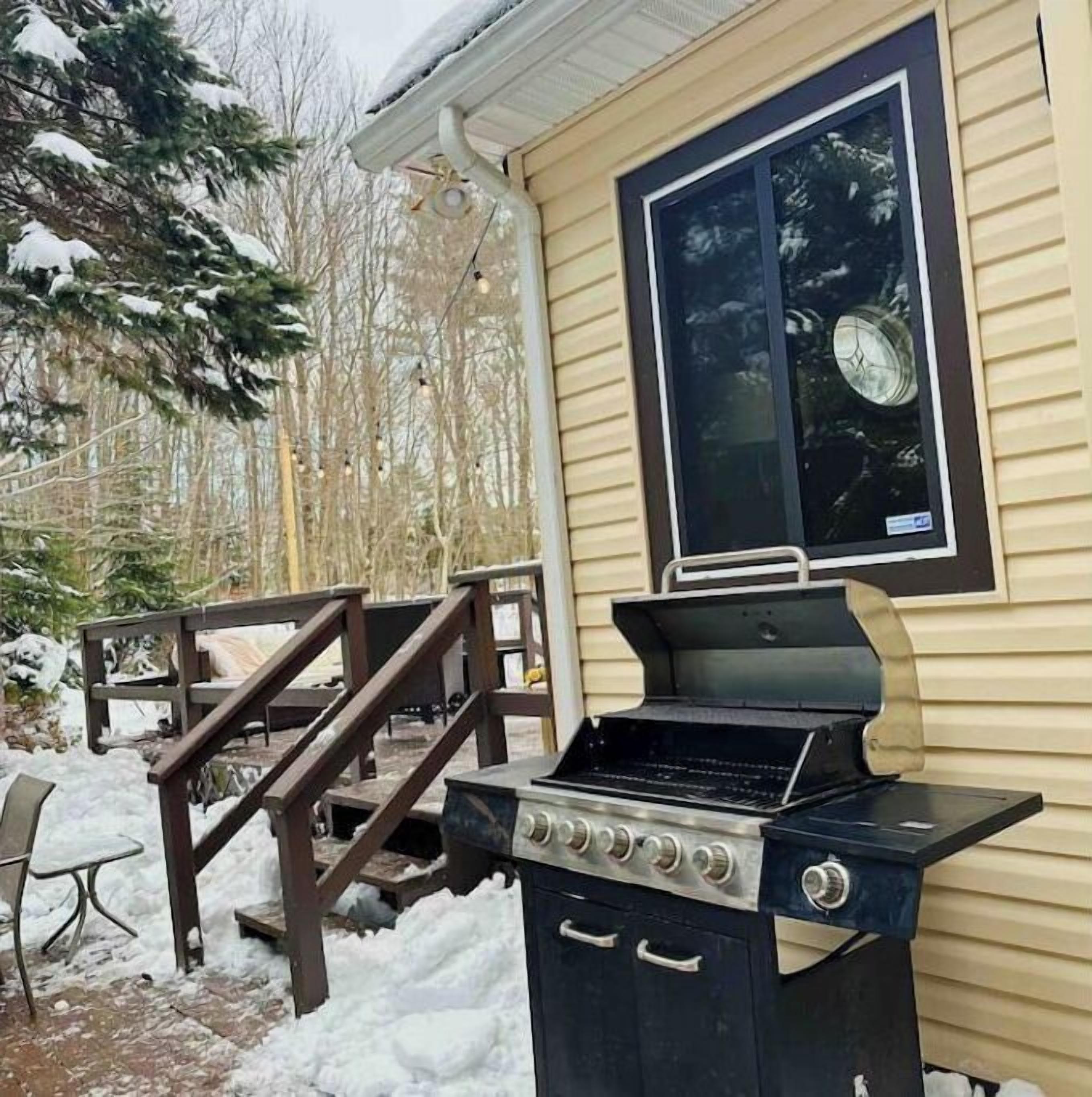 A backyard with a grill, wooden deck, and snow-covered ground.