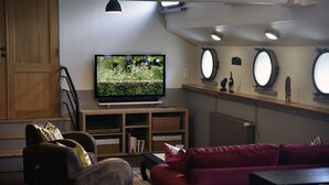 A living room with a television, a red sofa, a wooden cabinet, and a bookshelf. - Atypical accommodation on a barge (Ronquière)