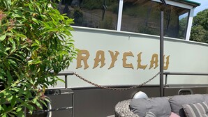 A boat named "RAYCLAU" with a wicker lounge area and a chain barrier. - Atypical accommodation on a barge (Ronquière)