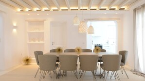 A modern dining room with a white table and grey chairs, a wooden ceiling, and pendant lights. - ISholidays Mykonos Villa Zircon (Tourlos)