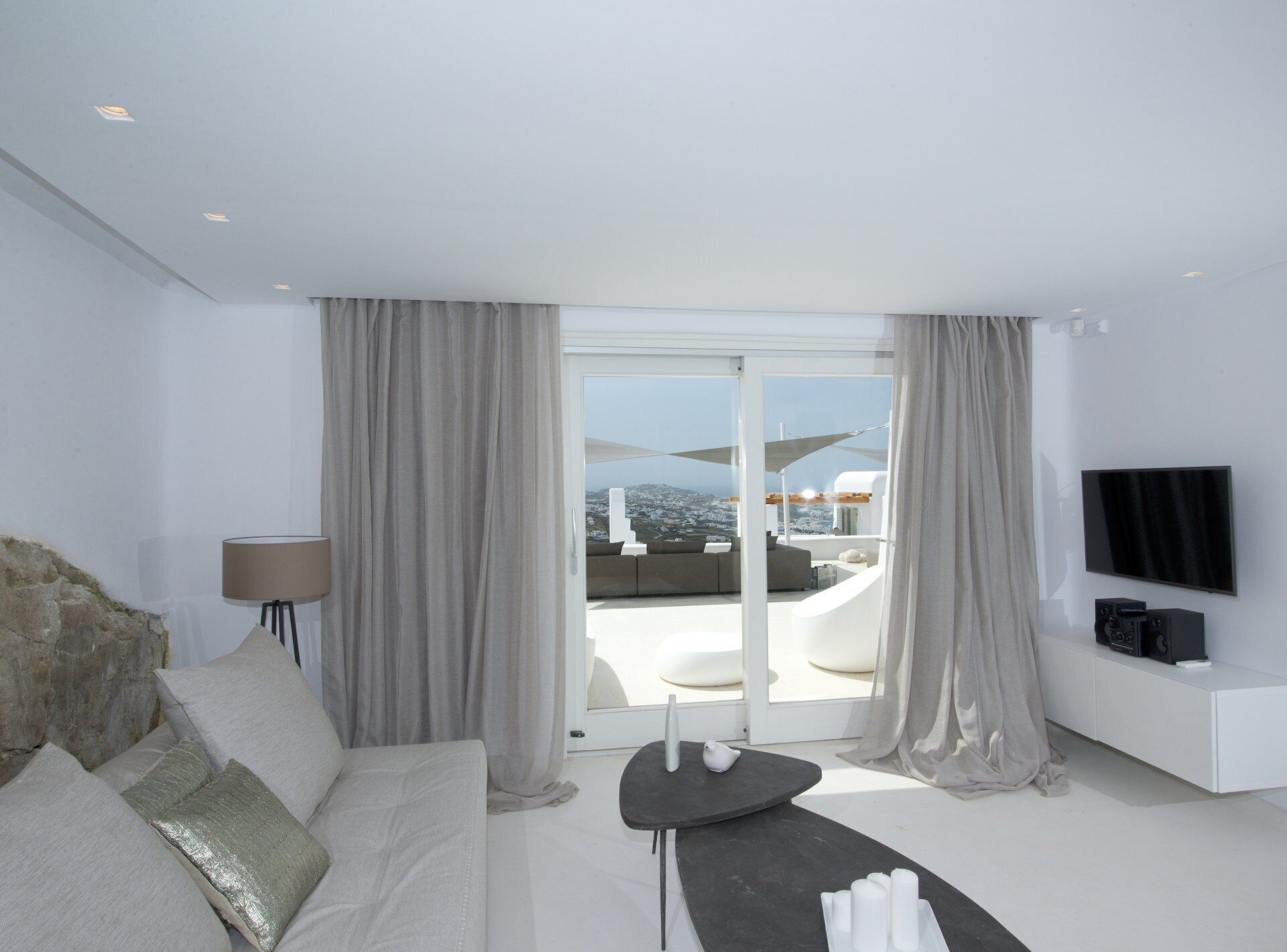 A modern hotel room with a large sliding glass door leading to a balcony with a city view.