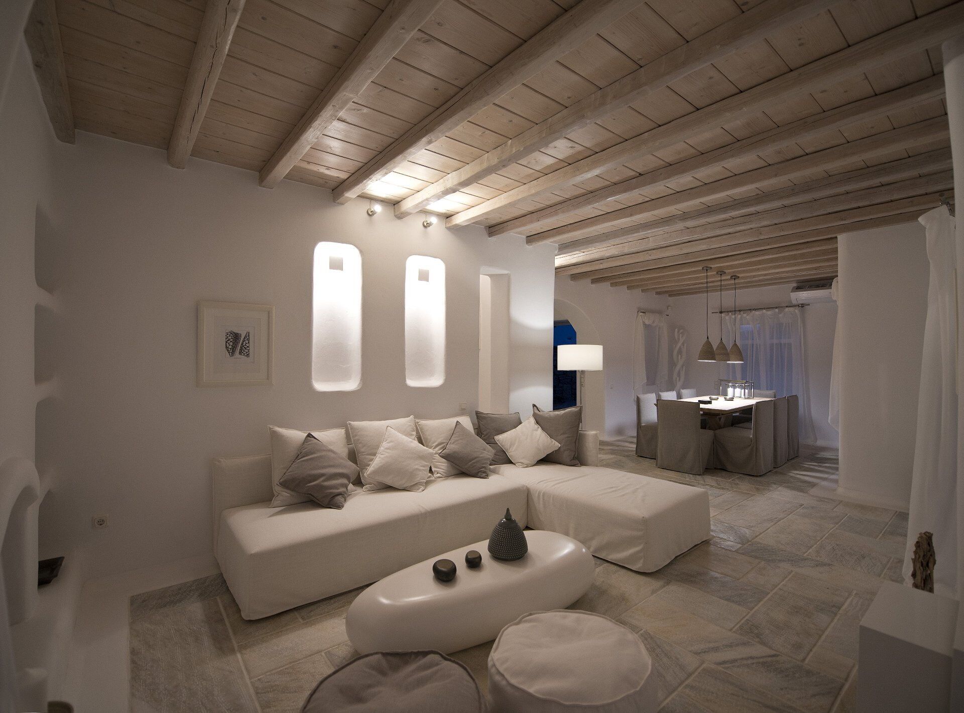 A modern living room with a white sofa, ottoman, and a dining area with a table and chairs.