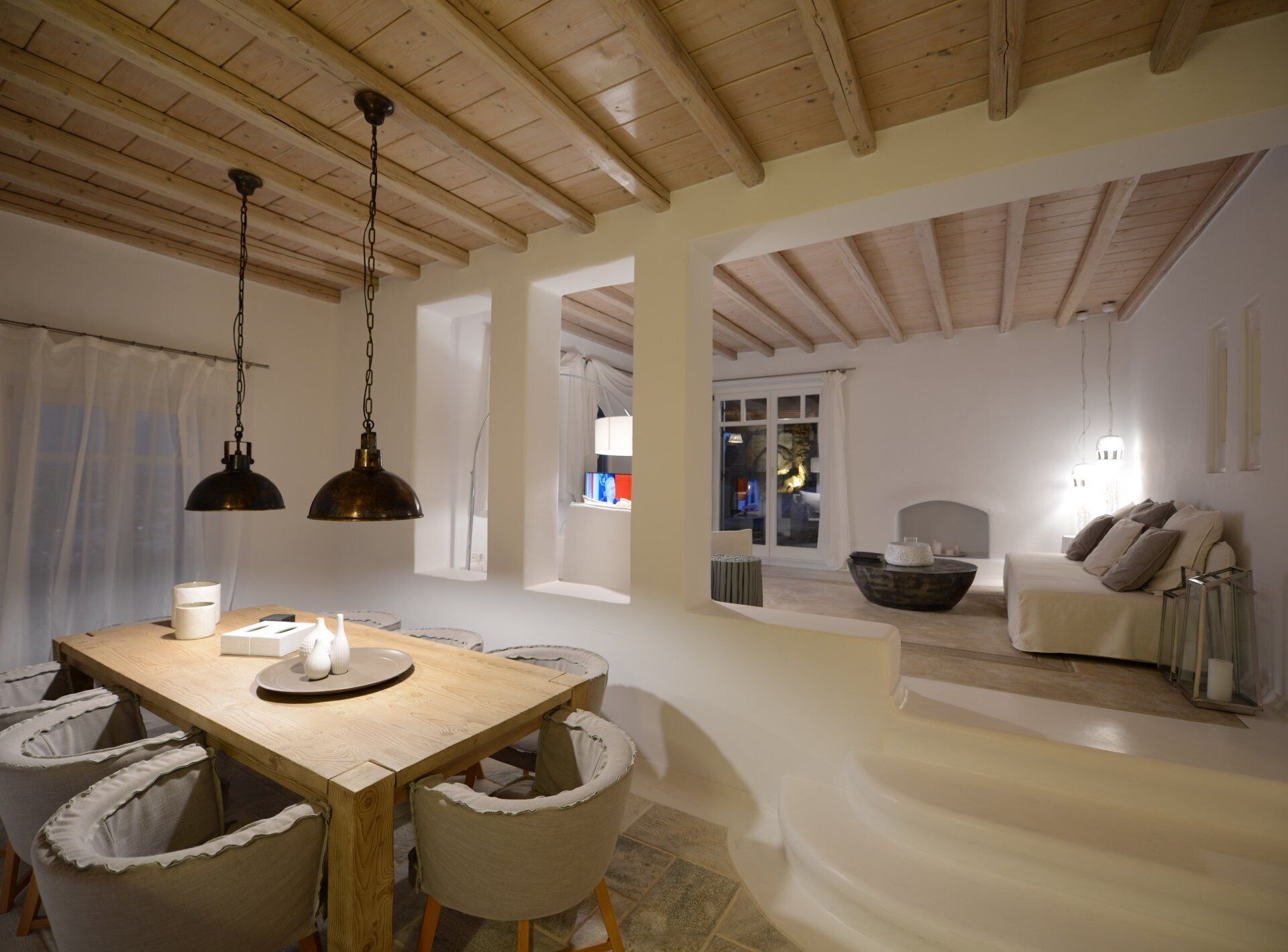 A dining area with a wooden table and chairs, a chandelier, and a view of a living room with a sofa and a fireplace.