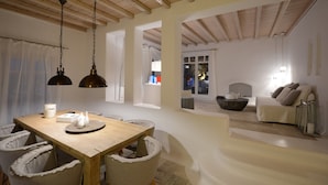 Un coin repas avec une table et des chaises en bois, un lustre et une vue sur un salon comprenant un canapé et une cheminée.