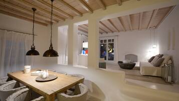 A dining area with a wooden table and chairs, a chandelier, and a view of a living room with a sofa and a fireplace.