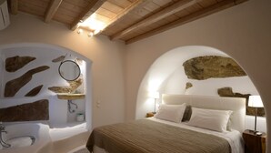 Une chambre avec un grand lit, une baignoire intégrée et un mur en pierre.