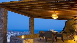 Un espace de restauration en plein air avec des murs en pierre, une pergola en bois et une vue sur la mer.