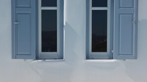 A building with two windows with blue shutters, a white exterior, and a light blue pool area. - ISholidays Mykonos villa Pearl (Ornos)