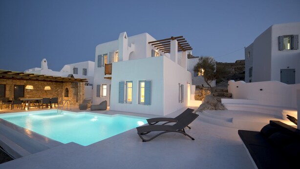 A modern white villa with a swimming pool, outdoor seating, and a stone wall. - ISholidays Mykonos villa Pearl (Ornos)