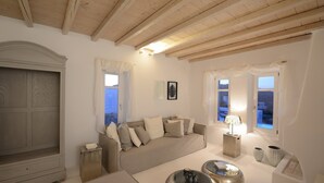 A spacious living room with a high wooden ceiling, a large window, and a cozy sofa. - ISholidays Mykonos villa Pearl (Ornos)