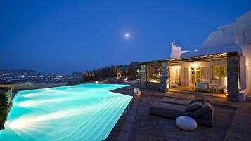 Una villa moderna con piscina, architettura in pietra e vista sulla città al crepuscolo.