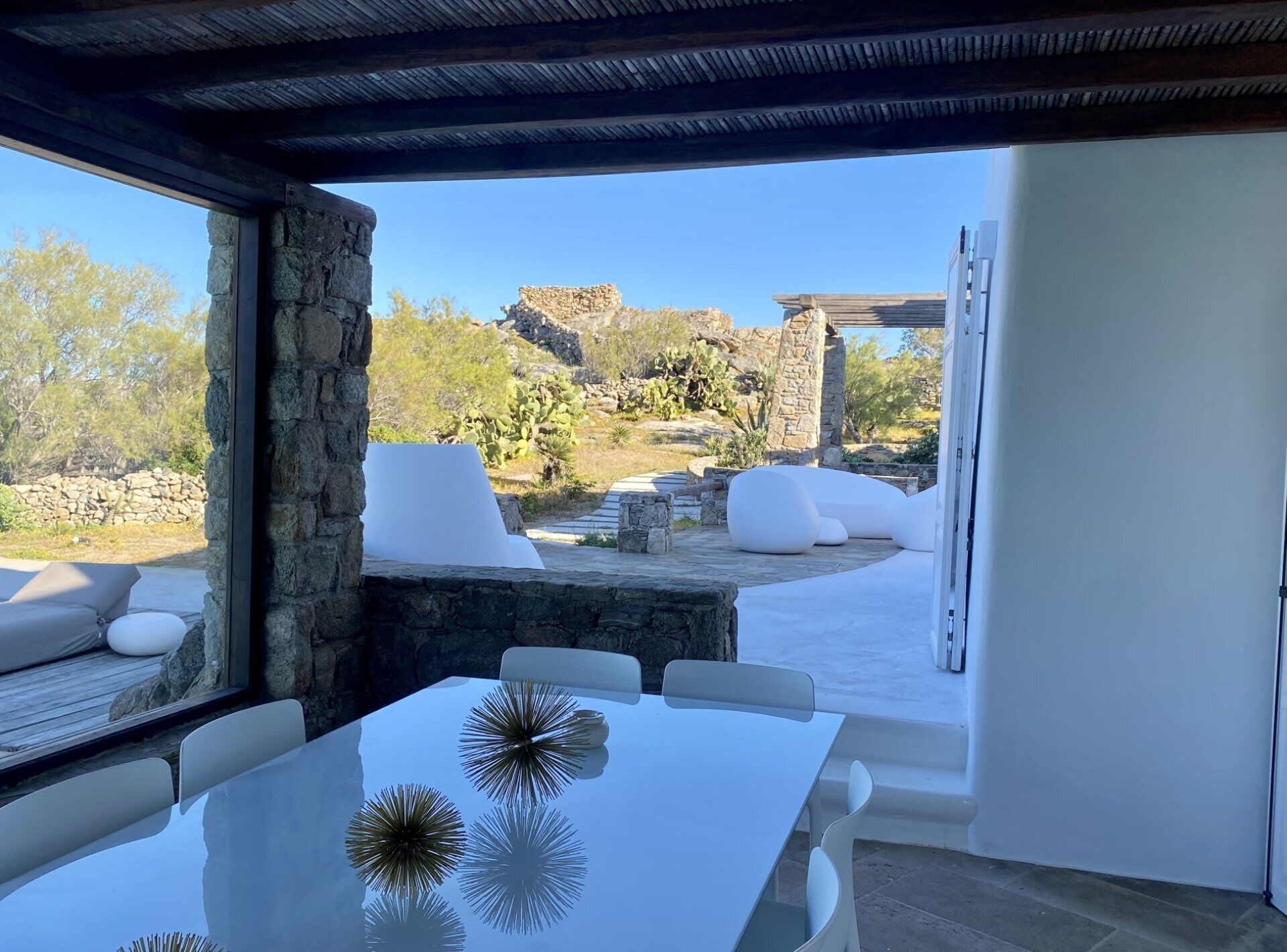 Una zona pranzo all'aperto moderna con pareti in pietra, arredi bianchi e vista su un paesaggio roccioso.