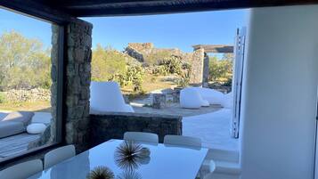 Una zona pranzo all'aperto moderna con pareti in pietra, arredi bianchi e vista su un paesaggio roccioso.