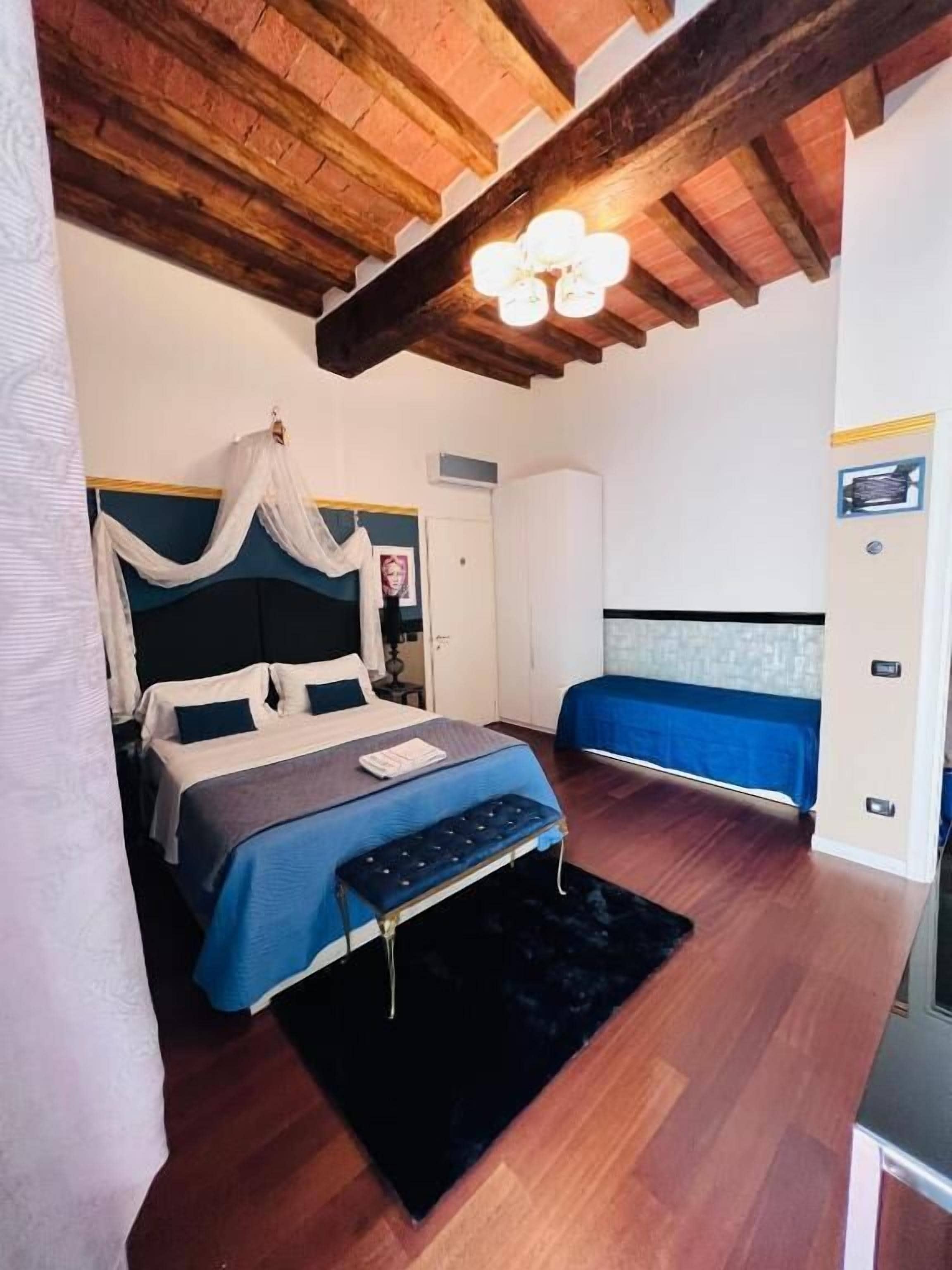 A bedroom with a bed, bedside tables, a bench, and a ceiling with exposed beams.