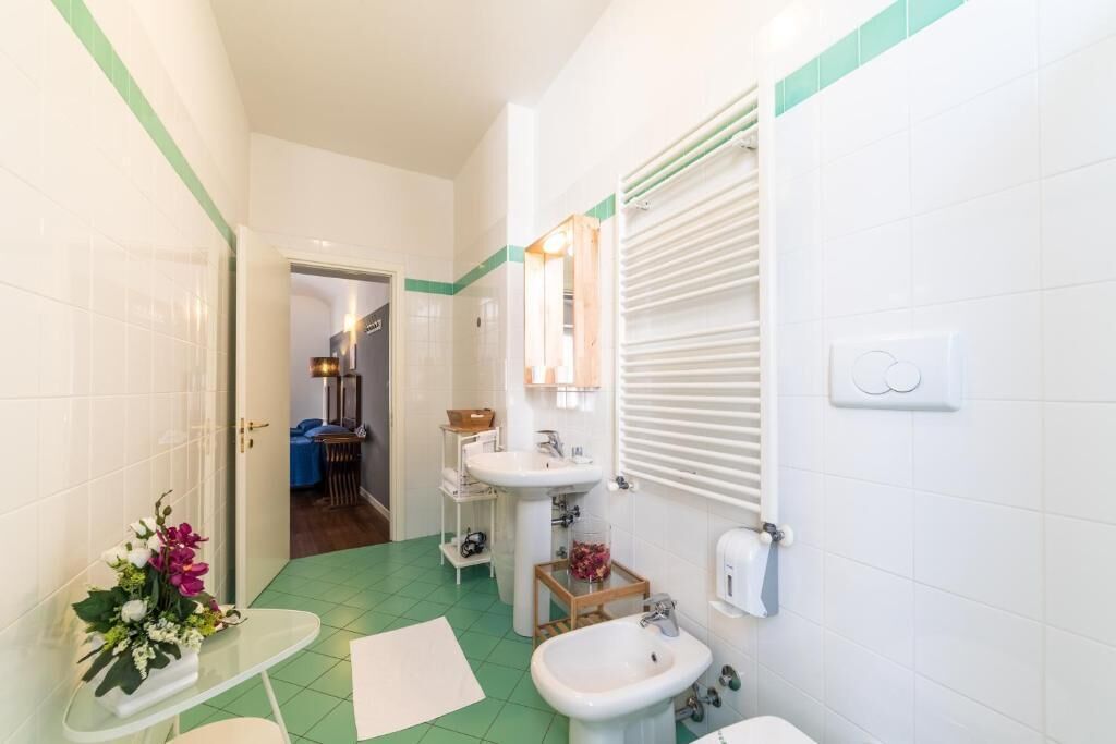 A bathroom with a green floor, white tiles, a sink, a bidet, and a mirror.