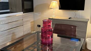 Eine moderne Küche mit einem Esstisch aus Glas, einer rosafarbenen Vase, einem Fernseher und Holzschränken.