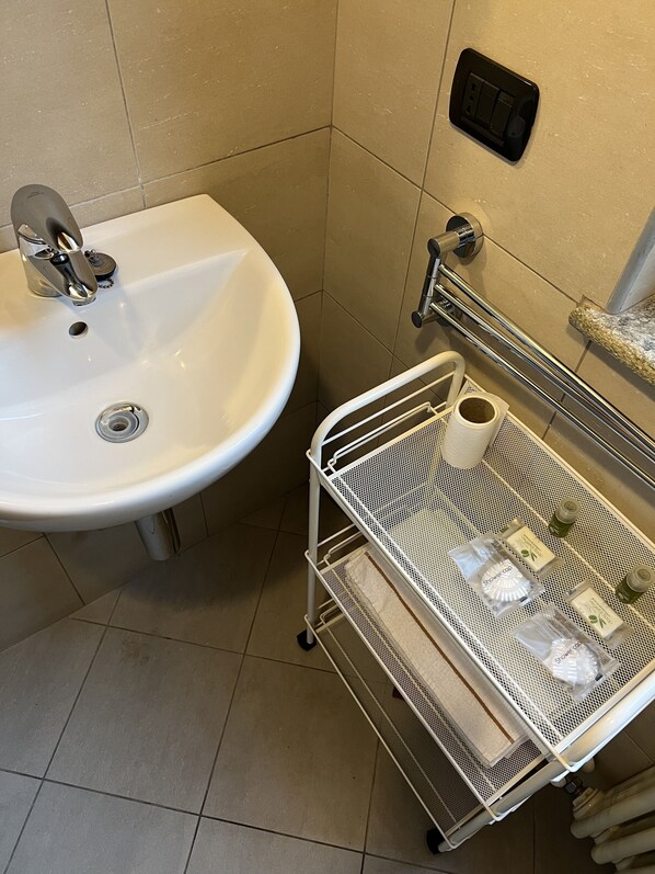 Une salle de bain avec un lavabo blanc, une colonne de douche en métal et un porte-serviettes.