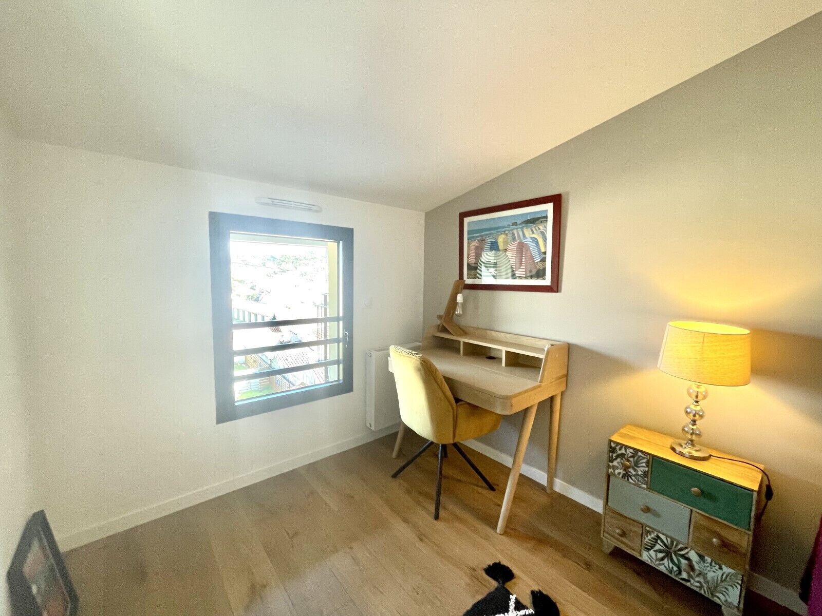 A room with a desk, chair, lamp, and a framed picture on the wall.