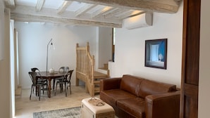 A cozy living room with a brown leather sofa, a wooden dining table with chairs, a staircase, and a framed picture on the wall. - House with full aircon within yards of centre of Meursault. (Meursault)