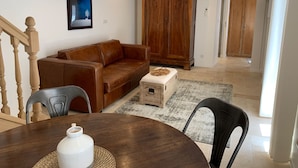 A living room with a brown leather sofa, a wooden cabinet, a dining table with chairs, and a painting on the wall. - House with full aircon within yards of centre of Meursault. (Meursault)