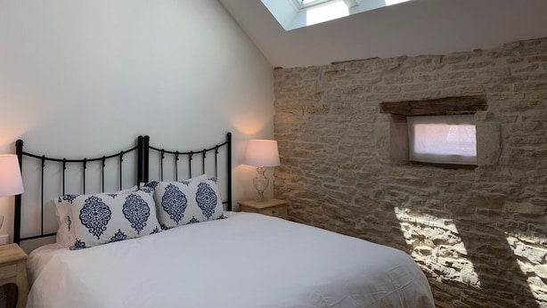 A bedroom with a stone wall, a bed with patterned pillows, two bedside lamps, and skylights. - House with full aircon within yards of centre of Meursault. (Meursault)