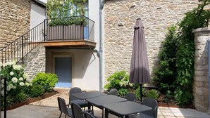 A courtyard with a stone wall, a wooden balcony with plants, a table with chairs, and an umbrella. - House with full aircon within yards of centre of Meursault. (Meursault)
