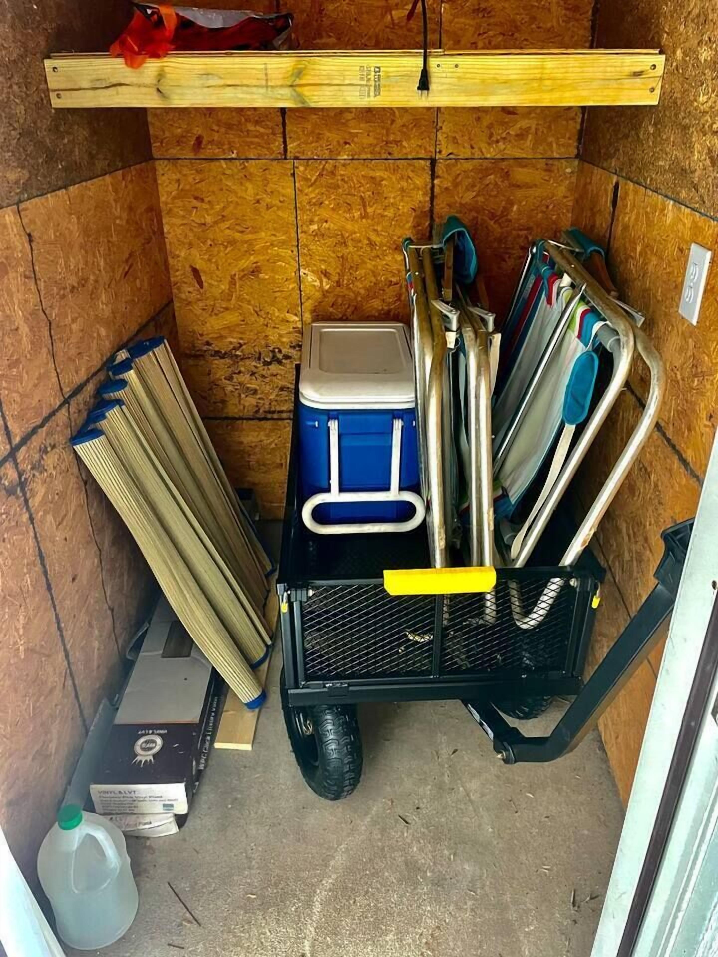 Een opslagruimte met een zwarte trolley met schoonmaakartikelen, een blauwe koelbox en een waterkan.
