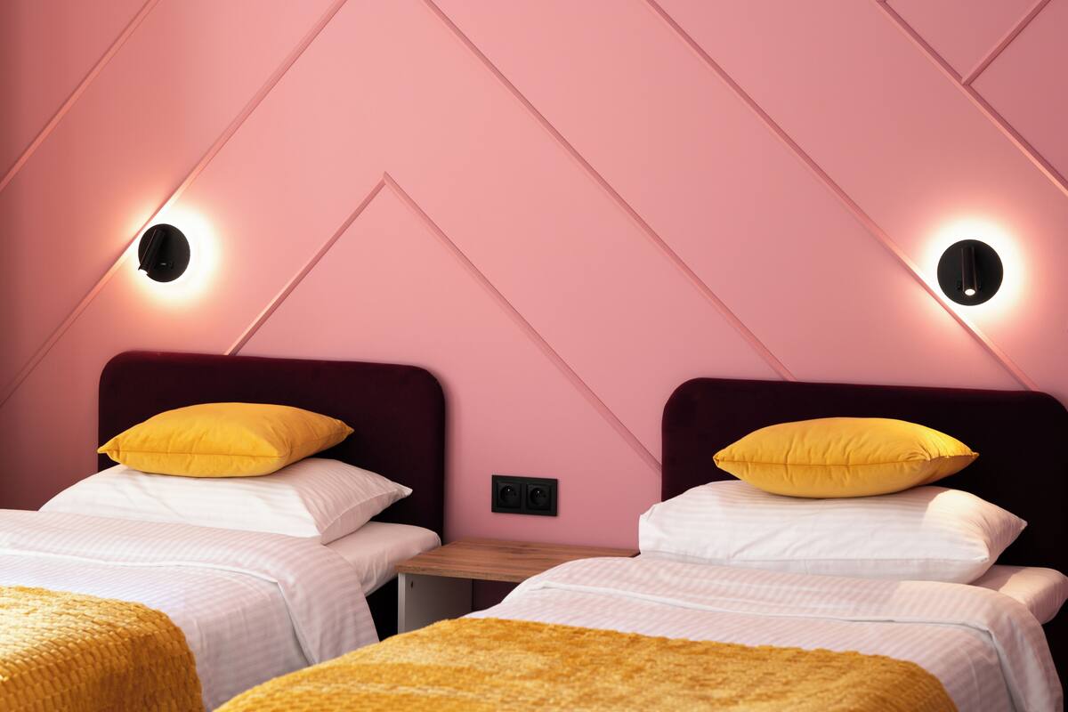 A hotel room with two beds, each with a yellow pillow, and a small wooden table between them.
