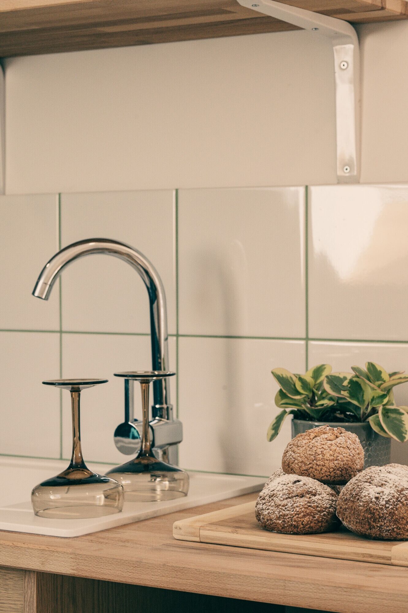 A kitchen with a stainless steel faucet, a glass wine glass, and a wooden cutting board with bread.