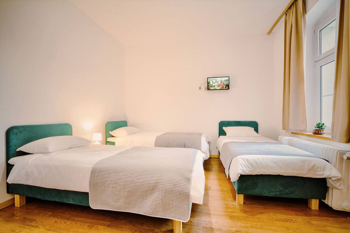 A room with two beds, each with a green headboard, white bedding, and a small bedside table with a lamp.