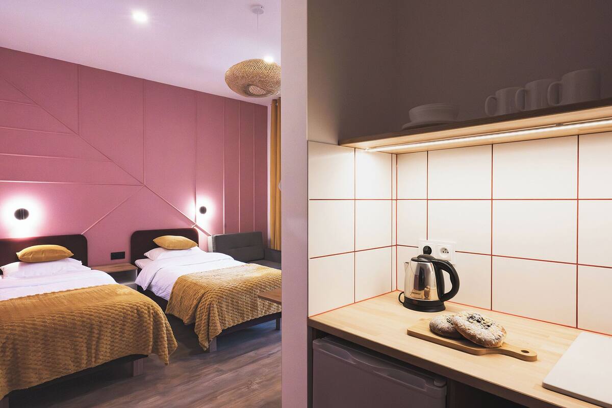 A hotel room with two beds, a kitchenette, and a modern design.