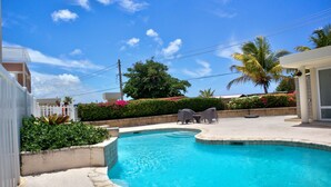 A swimming pool with a curved edge, surrounded by a landscaped area with plants and a palm tree.