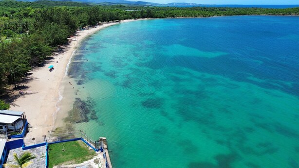 A beach with clear turquoise waters, a sandy shore, and dense greenery.