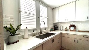 A modern kitchen with white cabinets, a sink, and a window with blinds.