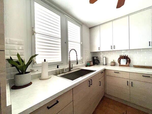 A modern kitchen with white cabinets, a sink, and a window with blinds.