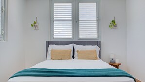 A neatly made bed with white bedding and a teal throw blanket, a bedside table with a lamp, and two wall-mounted planters with green plants.